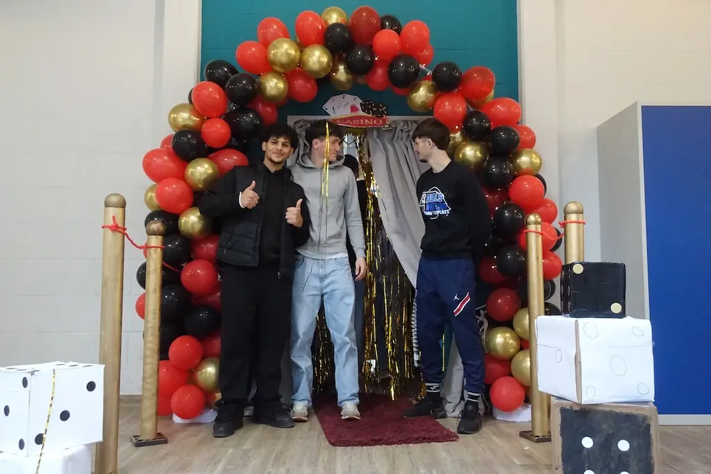 Drei Jugendliche posieren unter einem rot-schwarz-goldenen Ballonbogen