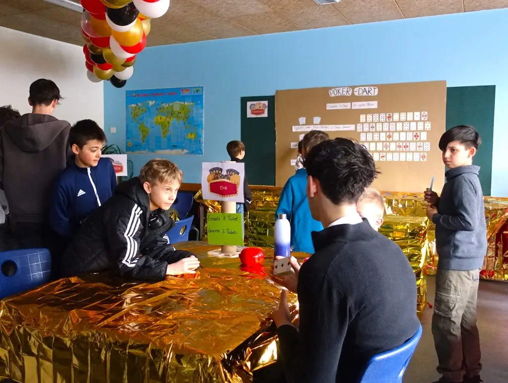 Jugendliche an einem Spieltisch mit goldener Dekoration in einem Klassenraum