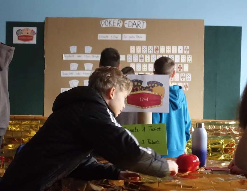 Schüler spielt an einem Tisch ein Wurfspiel, dahinter eine Spielwand