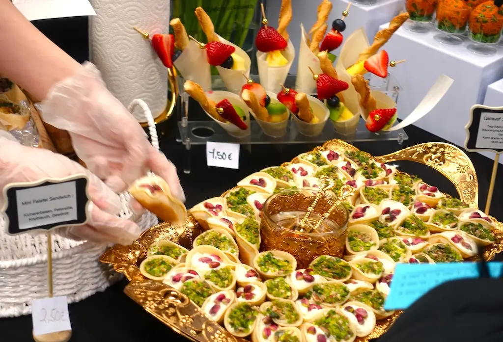 Hand mit Handschuh greift nach Häppchen auf einer Platte mit Fingerfood