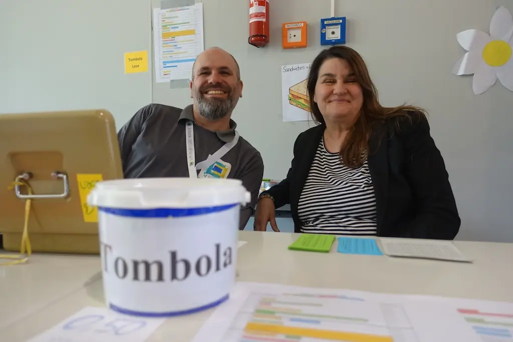 Mann und Frau sitzen an einem Tisch hinter einem Tombola-Eimer
