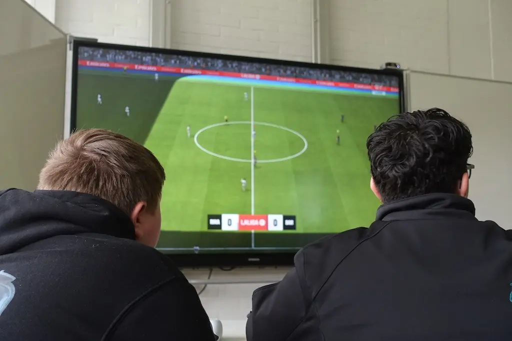Zwei Jugendliche spielen vor einem großen Bildschirm ein Fußball-Videospiel