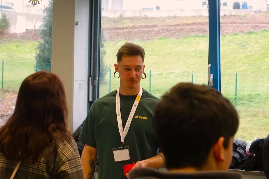 Junger Mann mit Namensband im Gespräch mit Jugendlichen vor einem Fenster