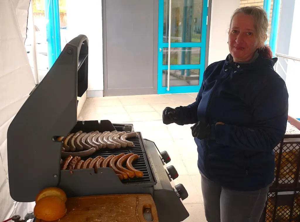 Frau steht an einem Grill mit Würstchen im Eingangsbereich der Schule