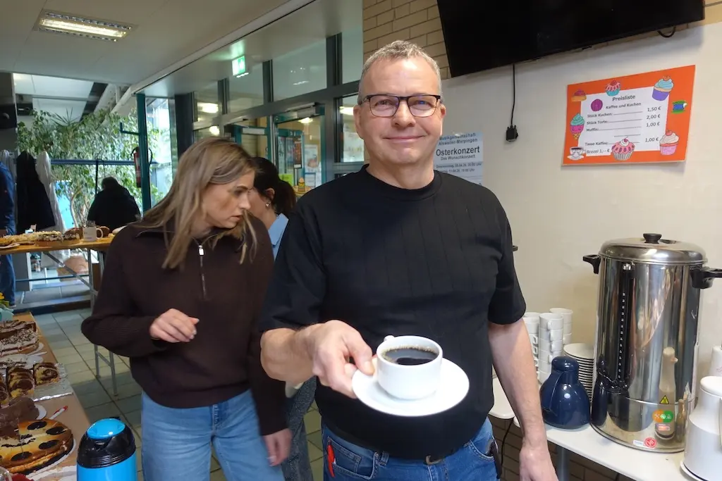 Mann reicht eine Tasse Kaffee an einem Getränkestand, daneben eine Frau