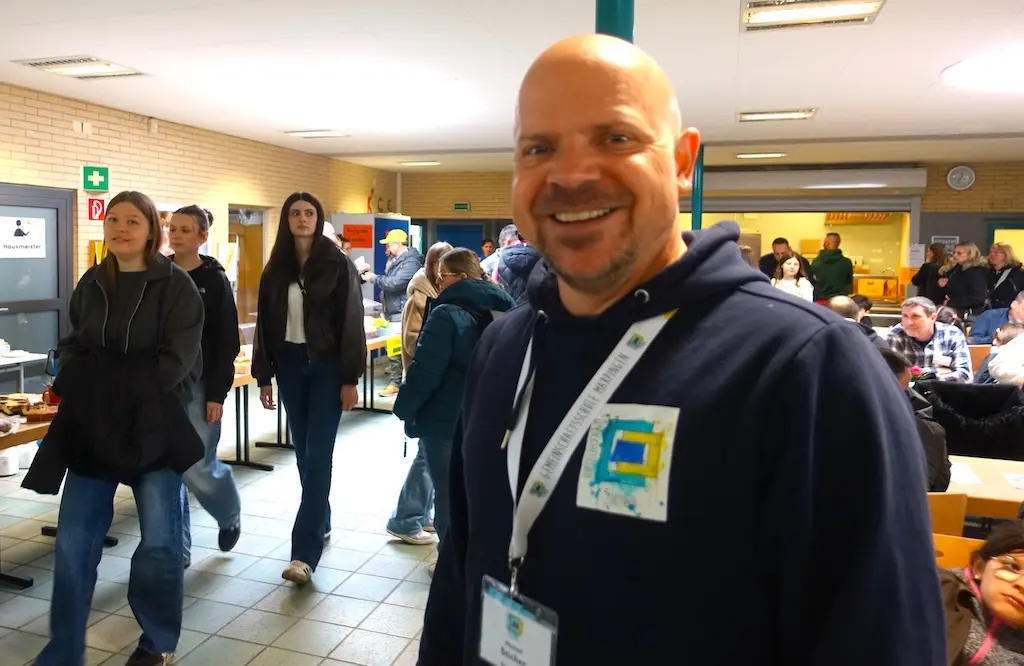 Lächelnder Mann mit Namensschild in einem belebten Flur der Schule