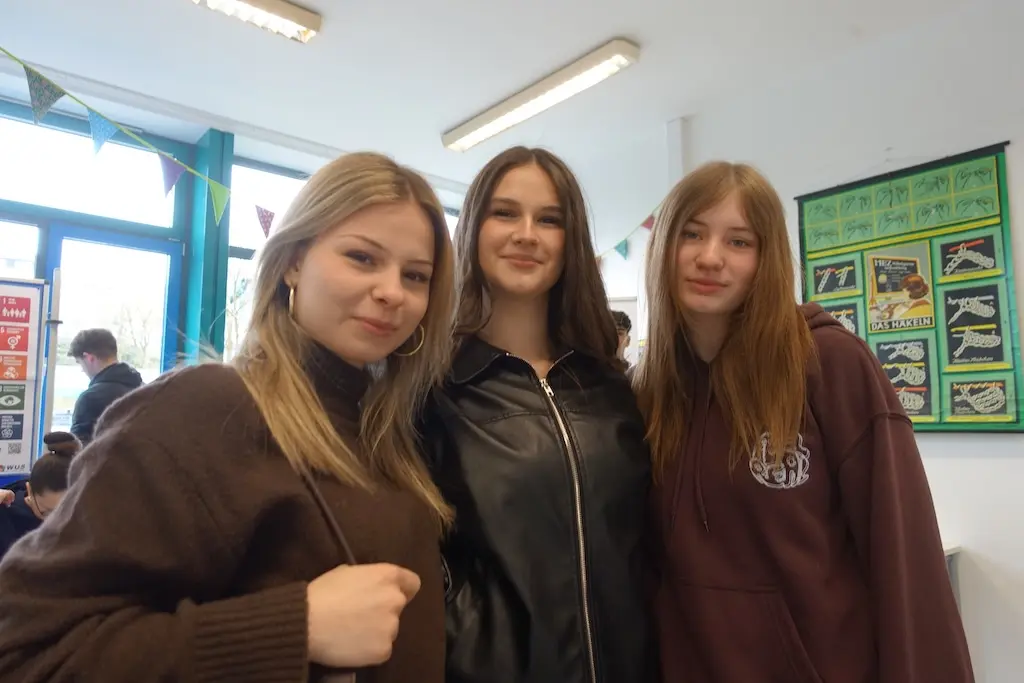 Drei Schülerinnen stehen nebeneinander und lächeln in die Kamera