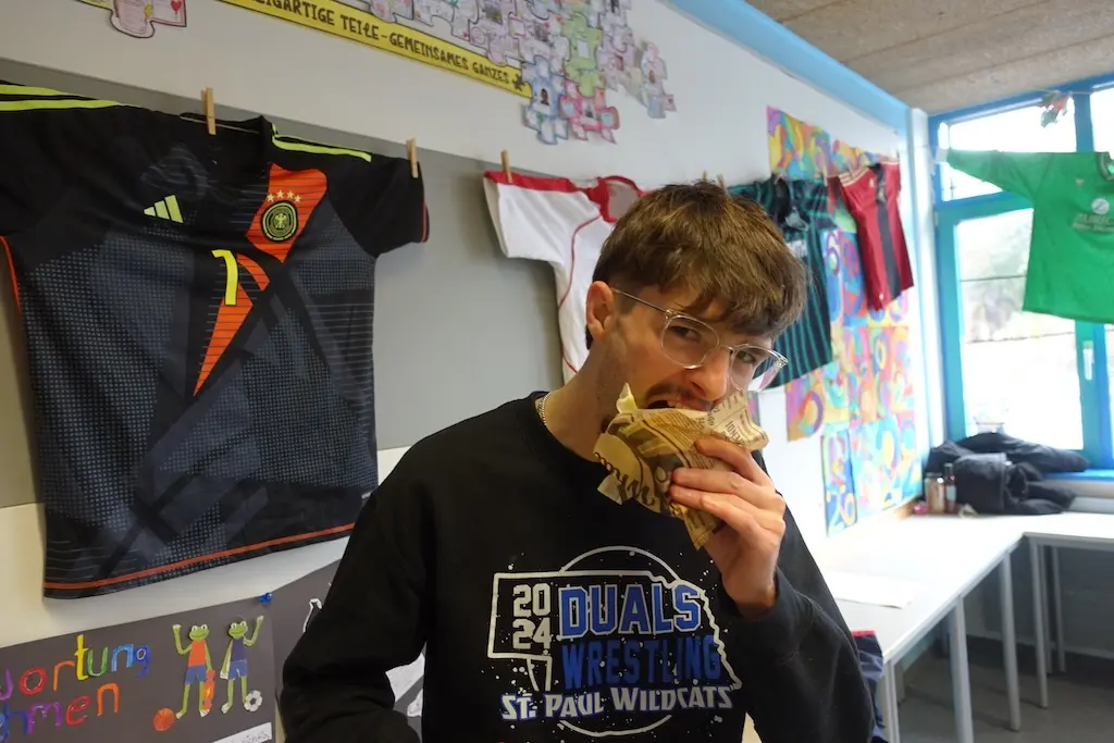 Schüler beißt in einen Snack, im Hintergrund hängen Trikots an der Wand