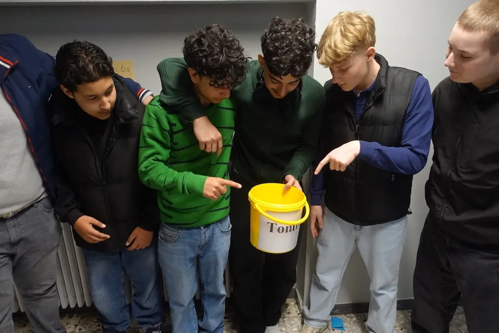 Gruppe Jugendlicher steht im Schulflur, einer hält einen gelben Eimer