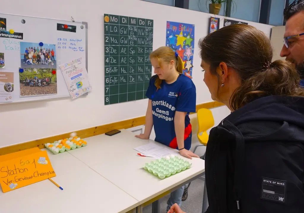 Jugendliche stehen an einem Tisch mit Spielen in einem Klassenraum mit Tafel