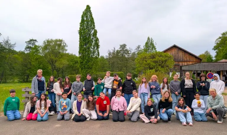 Große Gruppe deutscher und französischer Jugendlicher sitzt und steht im Freien vor Bäumen