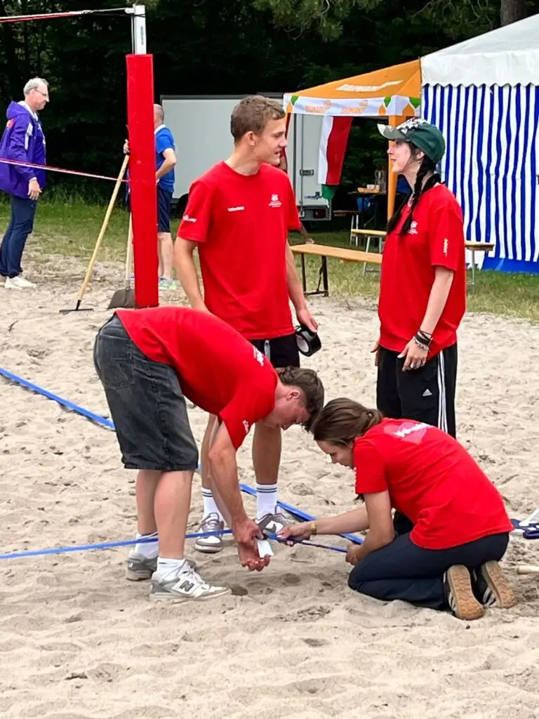 Jugendliche in roten Shirts helfen bei einer Sportveranstaltung auf einem Sandplatz