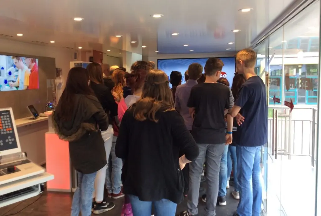 Schülergruppe steht im Inneren eines Ausstellungstrucks vor Bildschirmen