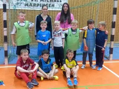 Kindergruppe mit Leibchen posiert mit zwei Betreuerinnen vor einem Tor in der Sporthalle
