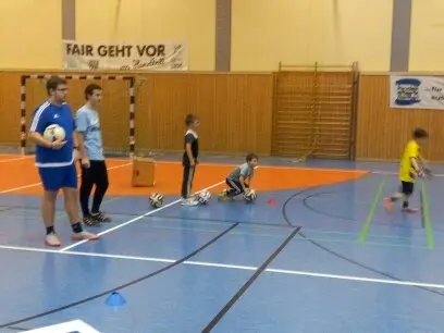 Junge Trainer leiten Kinder beim Fußballtraining in einer Sporthalle an