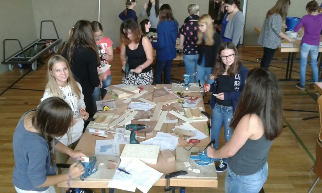 Gruppe von Schülerinnen und Schülern arbeitet gemeinsam an Tischen mit Papier und Bastelmaterial