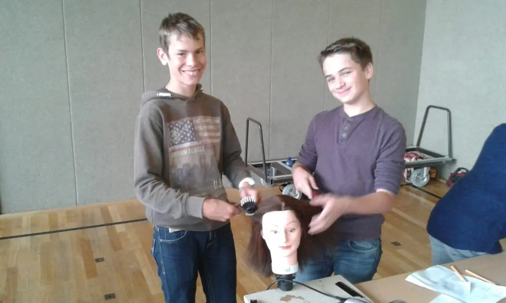 Zwei Schüler stehen an einem Tisch mit einem Frisierkopf und üben das Frisieren