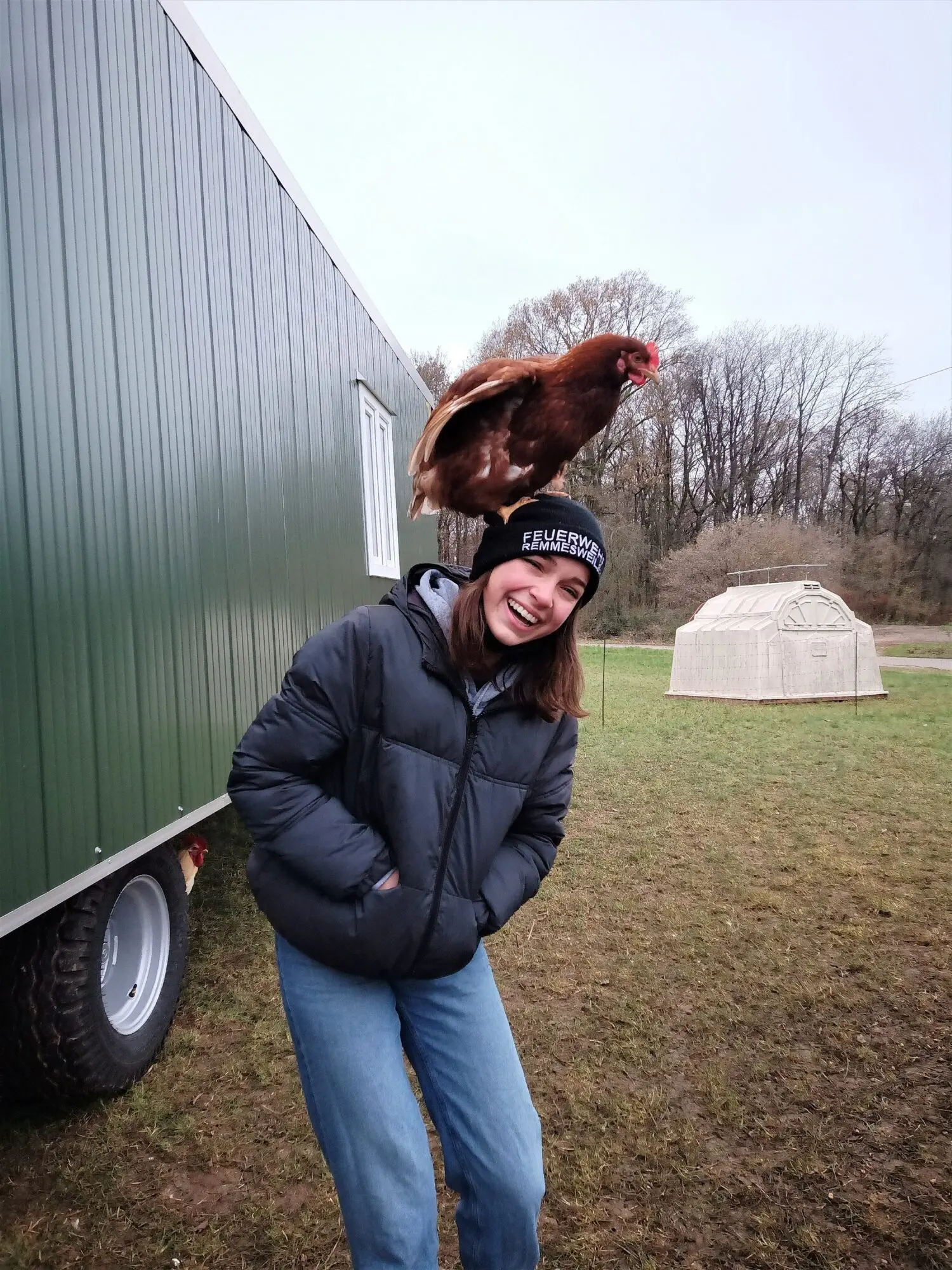 Jugendliche mit einem Huhn auf dem Arm auf einer Wiese neben einem Stallanhänger beim Besuch auf dem Biohof