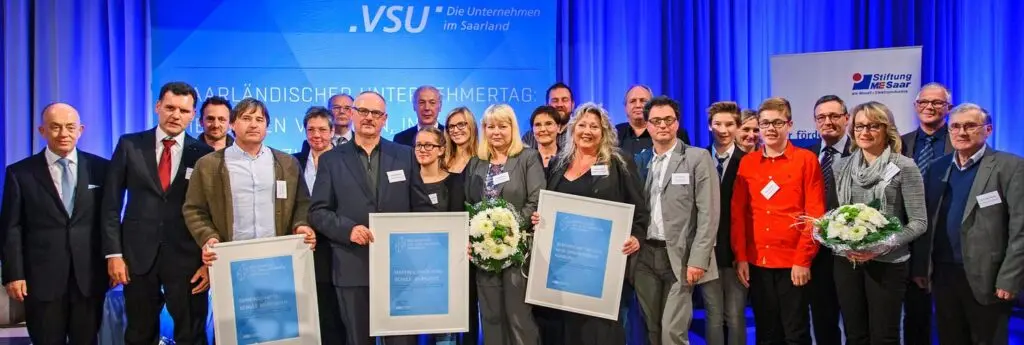 Gruppenfoto der Ausgezeichneten mit Urkunden und Blumen auf einer blau beleuchteten Bühne