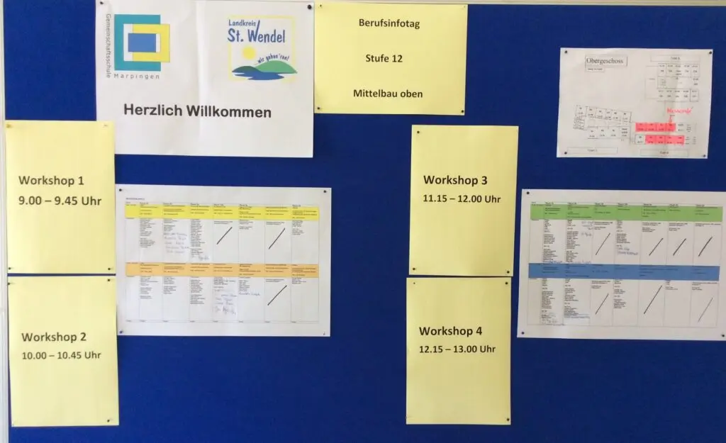 Blaue Stellwand mit Begrüßungsplakat und Aushängen zu Workshop-Zeiten