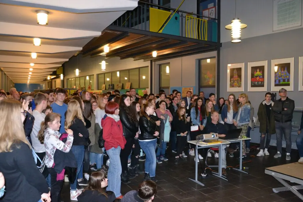 Volle Aula mit Schülerinnen und Schülern und Tischen bei einer Informationsveranstaltung