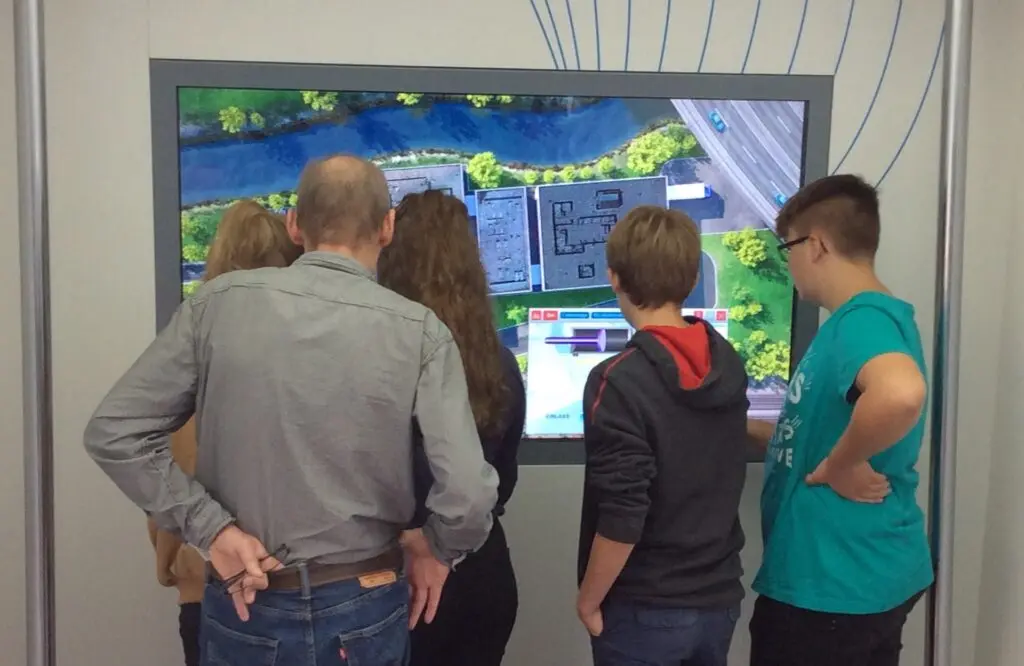 Jugendliche und ein Erwachsener schauen auf einen großen Touchscreen in einem Ausstellungsraum