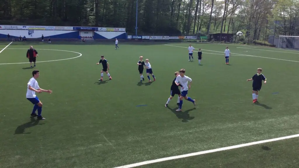 Fußballspiel von Schülerteams auf einem Kunstrasenplatz, Blick von der Seite