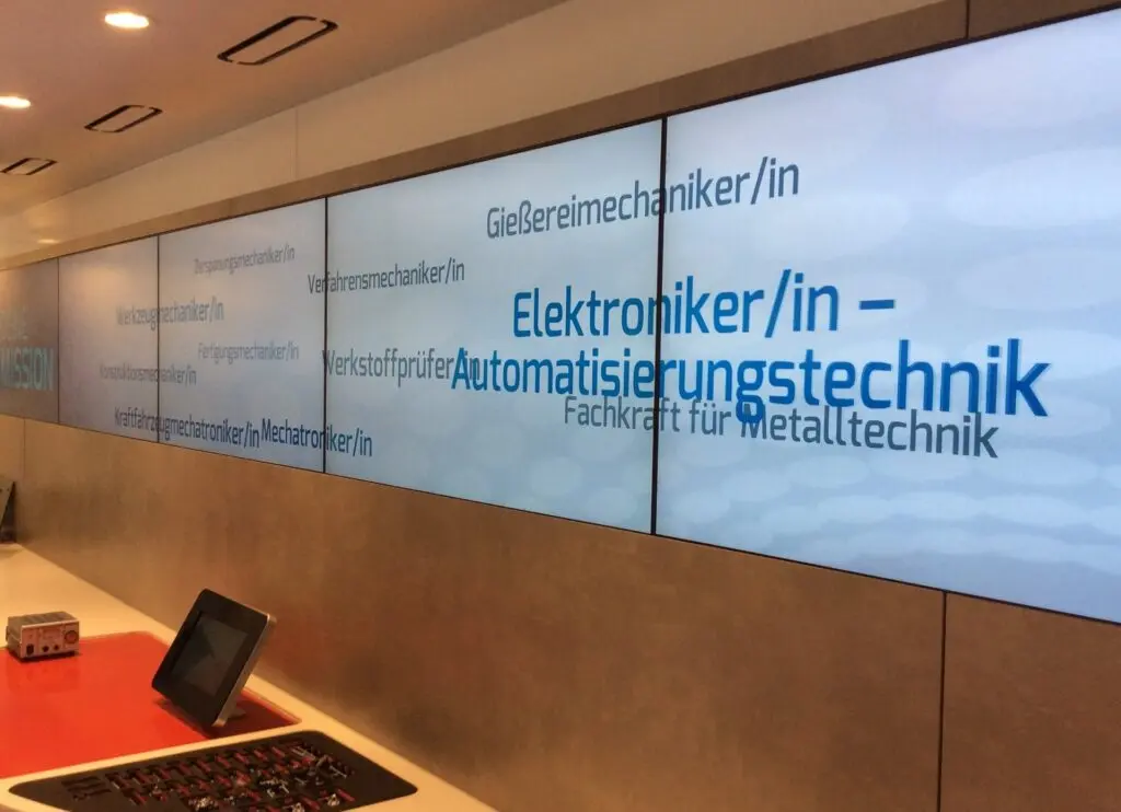 Videowand mit Berufsbezeichnungen wie Elektroniker/in für Automatisierungstechnik, davor Tablets