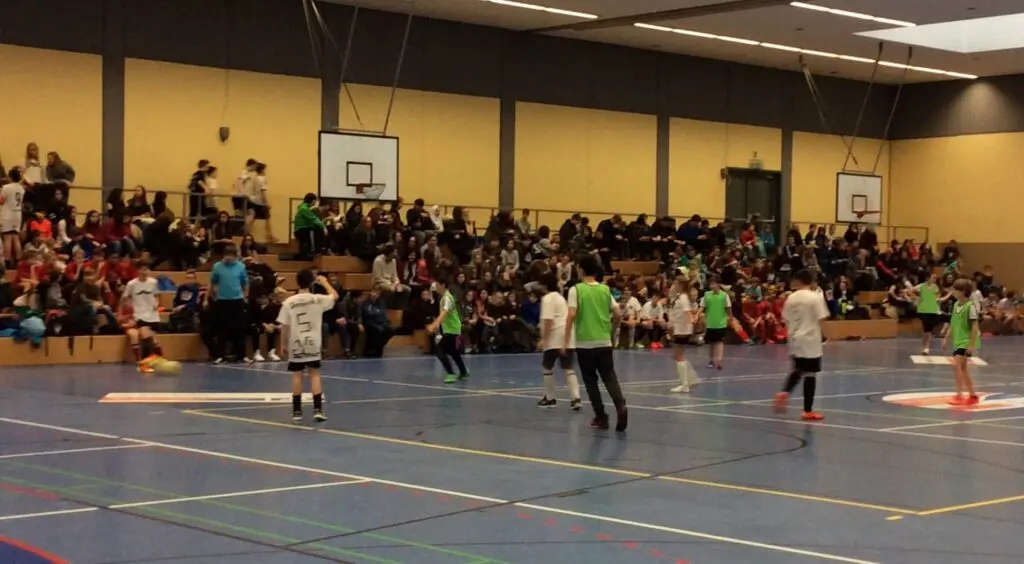 Spielszene eines Hallenfußballturniers mit Schülerinnen und Schülern, viele Zuschauer am Rand