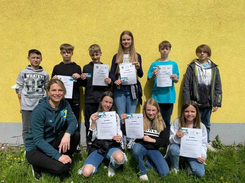 Schülerinnen und Schüler der Mediations-AG mit Urkunden vor einer gelben Wand auf dem Rasen