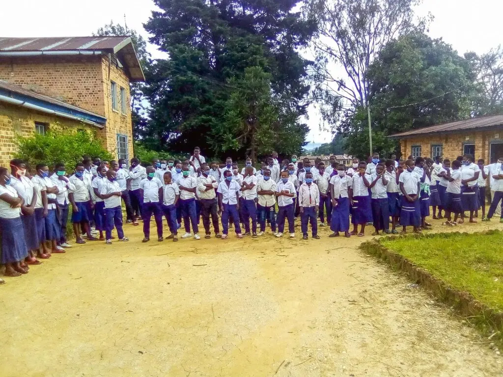 Große Gruppe von Kindern in blau-weißen Schuluniformen steht auf einem Platz vor Schulgebäuden in Afrika