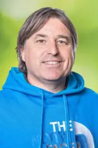 Porträt Thomas Alt, lächelnd im blauen Kapuzenpullover vor grünem Hintergrund