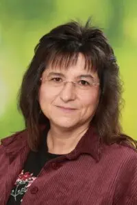 Porträt Anne Backes, mit dunklen Haaren und Brille vor grünem Hintergrund