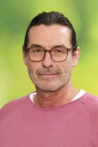 Porträt Gerd Bermann, mit Brille im rosa Pullover vor grünem Hintergrund