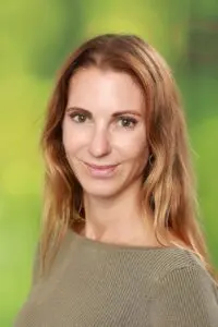 Porträt Nina Biehler, mit langen Haaren im olivfarbenen Oberteil vor grünem Hintergrund