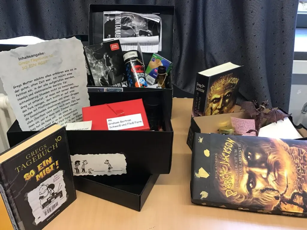 Lesekiste für das Fach Deutsch: geöffnete Kiste mit Buch, Briefen und kleinen Gegenständen auf einem Tisch