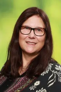 Porträt Andrea Christmann, mit dunklen Haaren und Brille vor grünem Hintergrund
