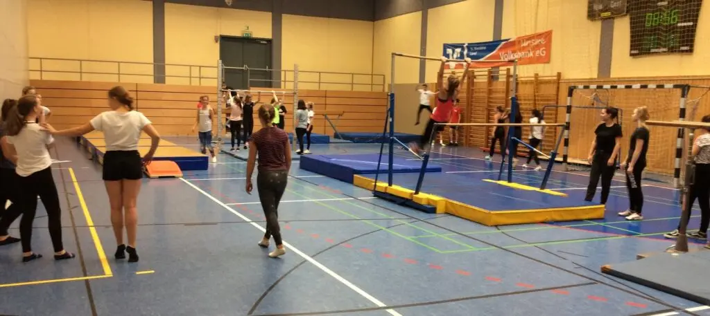 Kinder turnen an Matten und Geräten in einer Sporthalle mit Kletterwand