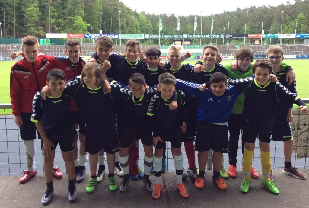 Schülerfußballmannschaft in dunklen Trikots posiert auf dem Sportplatz