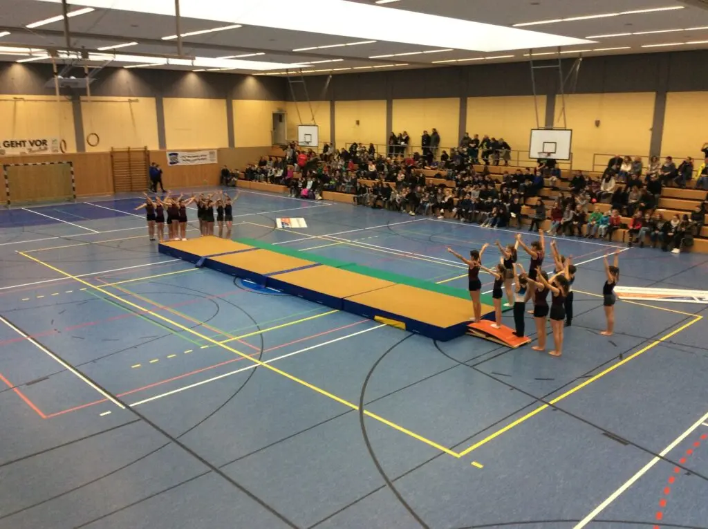 Sporthalle mit aufgebauten Mattenbahnen, Kinder warten an den Stationen, Zuschauer auf der Tribüne