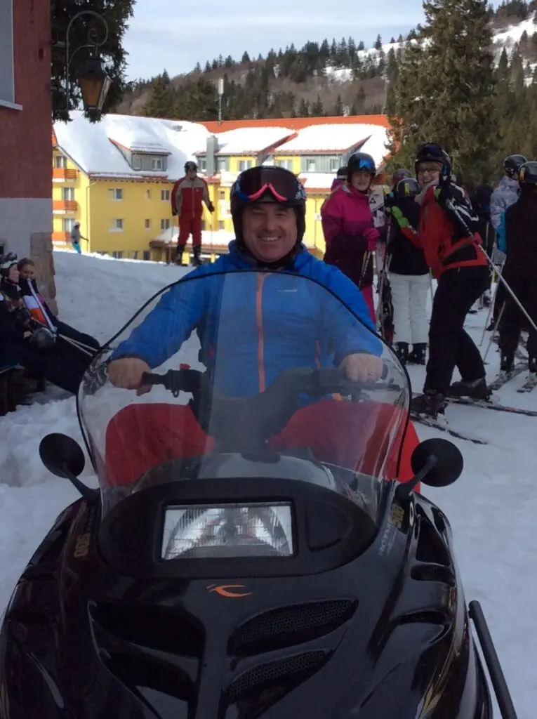 Person mit Helm fährt auf einem Schneemobil, dahinter Jugendliche im Schnee