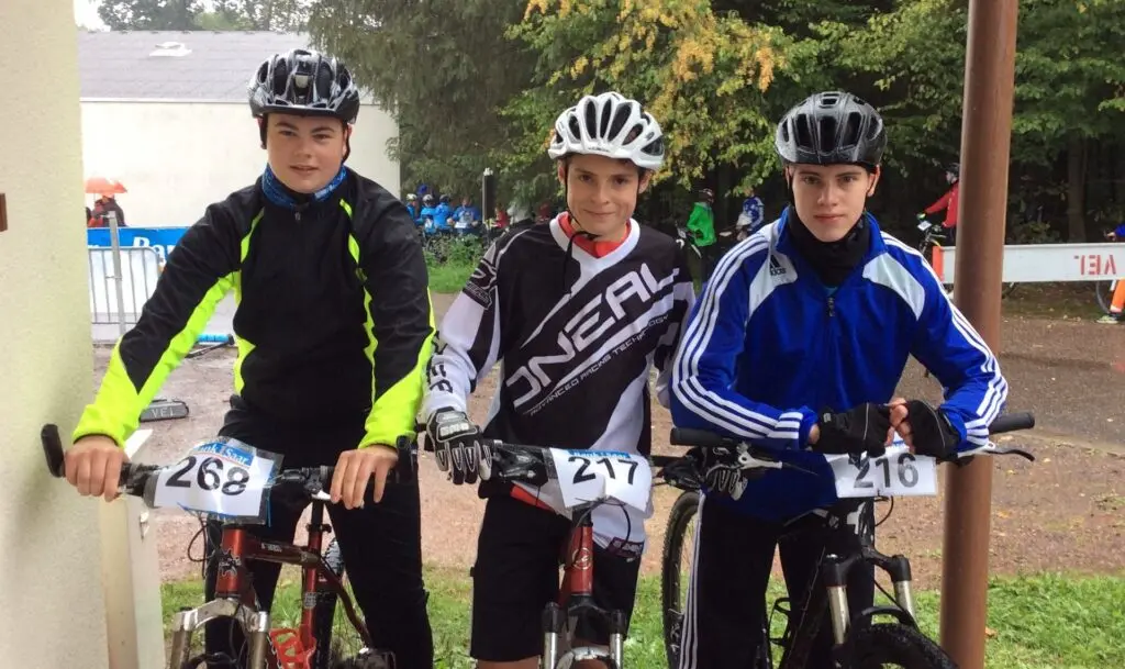 Drei Jugendliche mit Helmen und Startnummern auf Mountainbikes