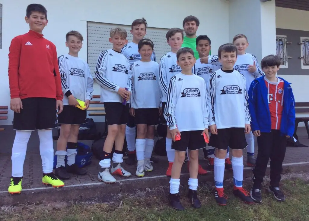 Schülermannschaft in weißen Shirts mit Betreuern vor einem Gebäude