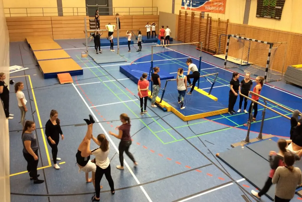 Kinder und Betreuende an einem Bewegungsparcours aus Matten und Geräten in der Sporthalle