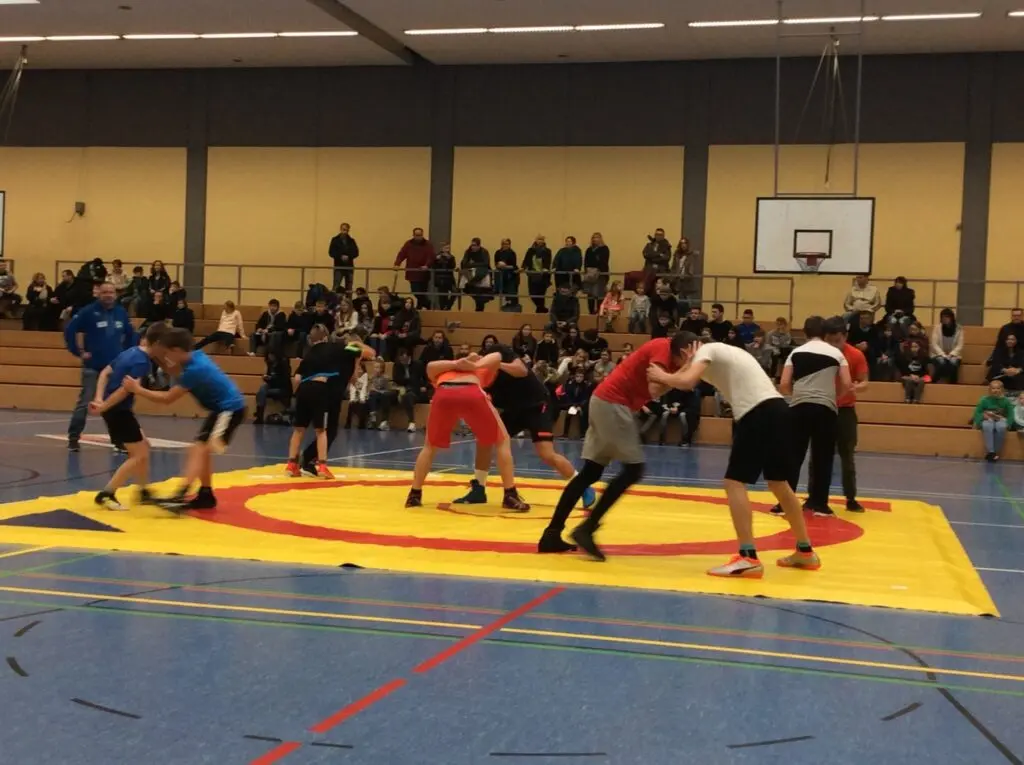 Mehrere Ringkämpfe auf einer Matte in einer Sporthalle, Zuschauer auf der Tribüne