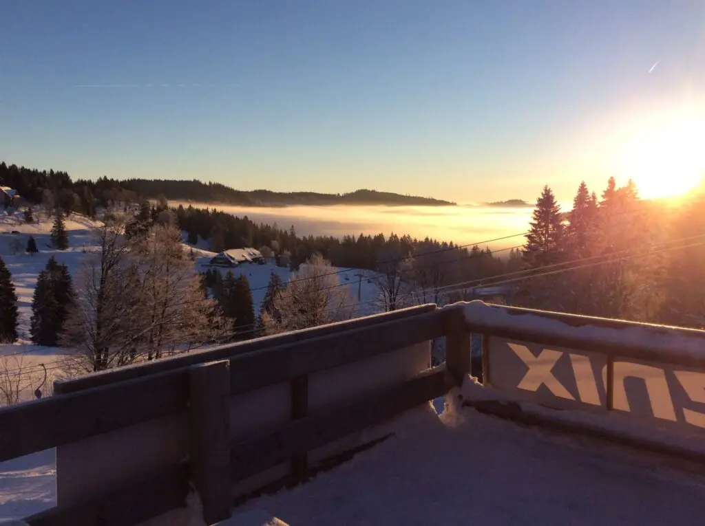 Sonnenaufgang über verschneiten Bergen und Wolkenmeer, gesehen von einem Holzbalkon