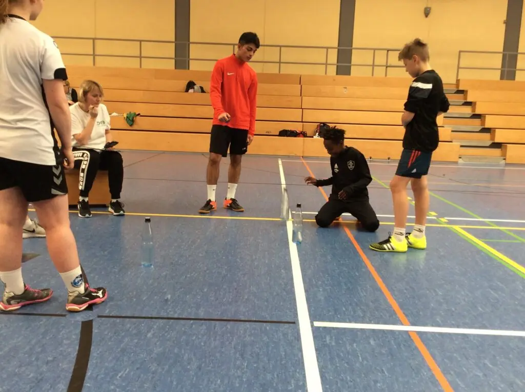 Schülerinnen und Schüler an einer Station in der Sporthalle, ein Junge kniet auf dem Boden, andere schauen zu