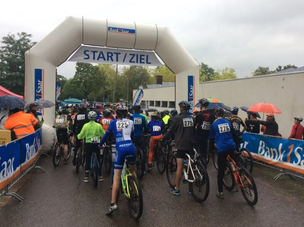 Mountainbikerinnen und -biker sammeln sich unter einem Start/Ziel-Bogen