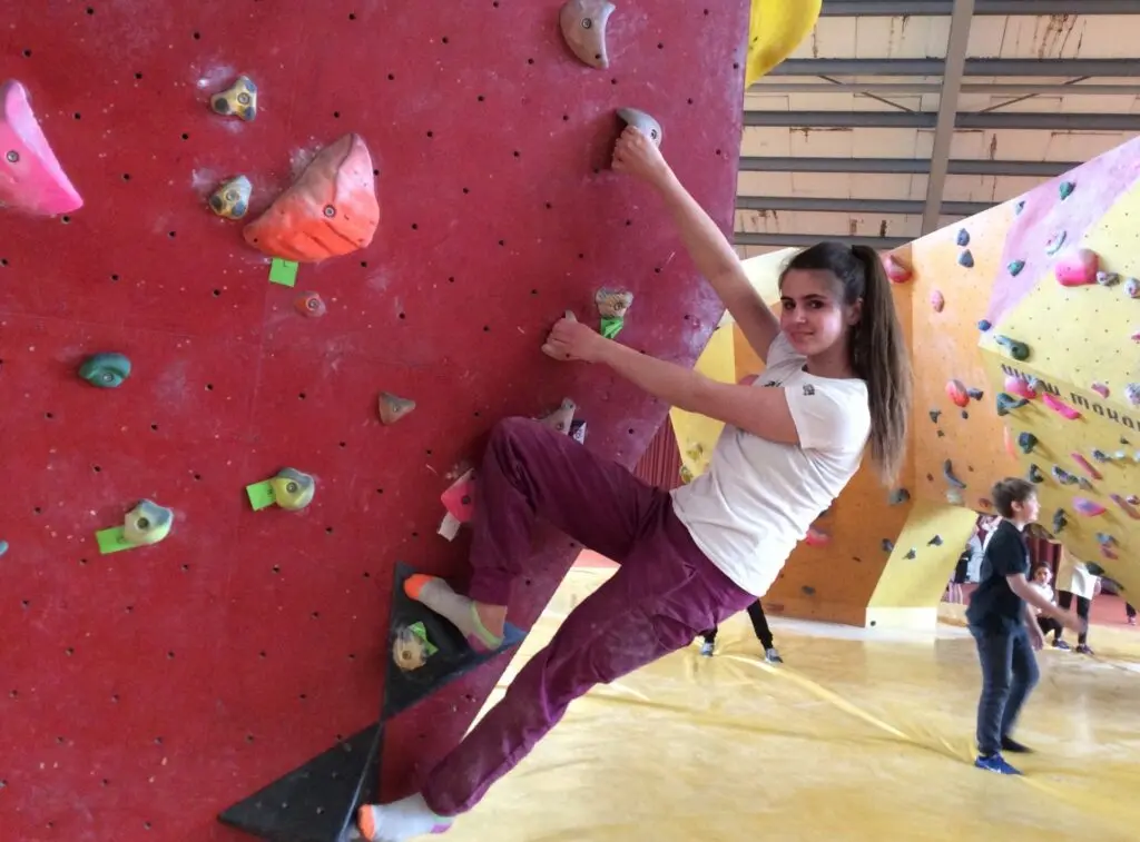 Schülerin klettert an einer roten Kletterwand in einer Halle