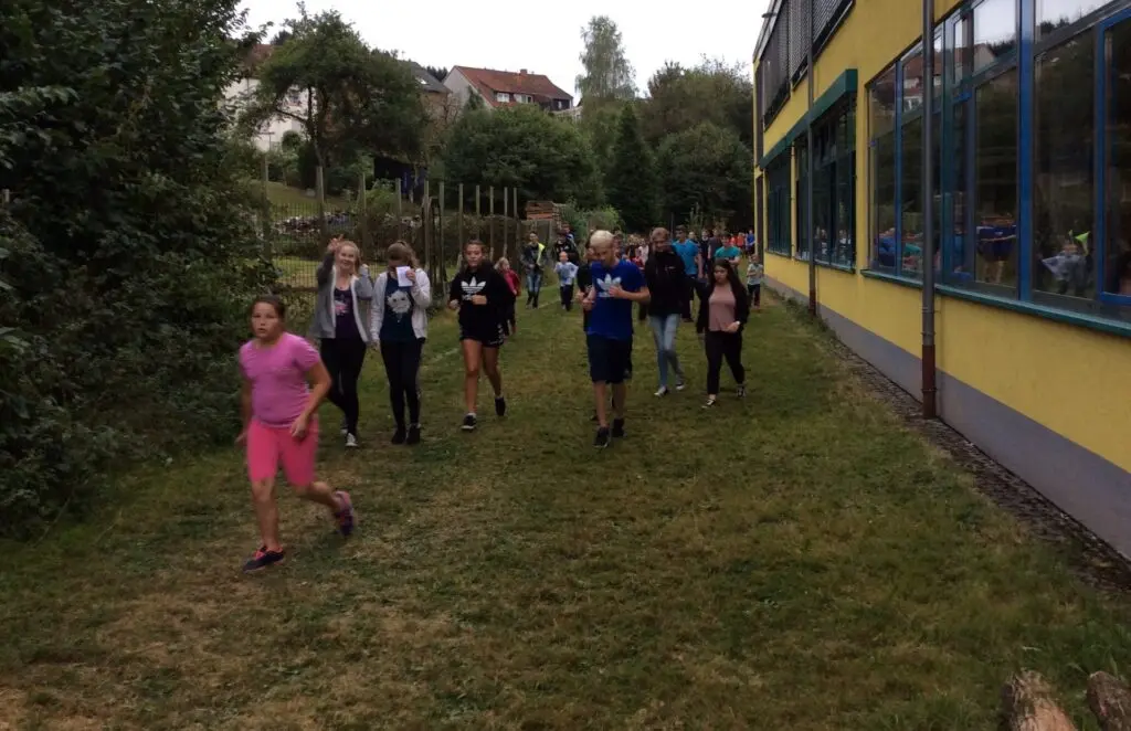 Läuferinnen und Läufer auf einer Wiese entlang des gelben Schulgebäudes